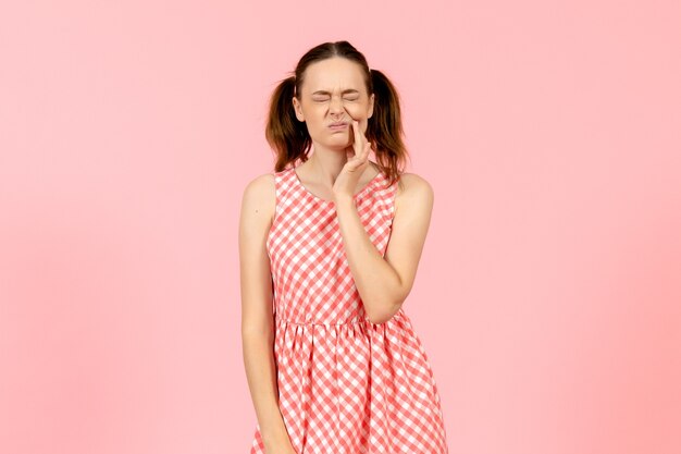 junges Mädchen im niedlichen rosa Kleid, das Zahnschmerzen auf rosa hat