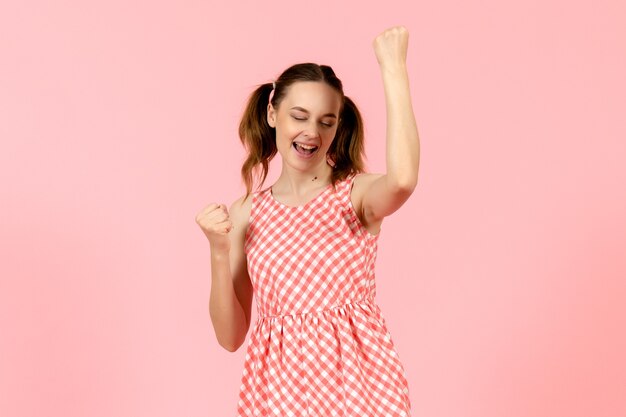 junges Mädchen im niedlichen rosa Kleid mit freudigem Ausdruck auf rosa