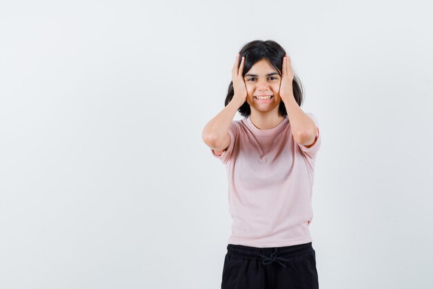 Junges Mädchen im rosa T-Shirt und in der schwarzen Hose, die Hände auf Kopf halten und glücklich schauen