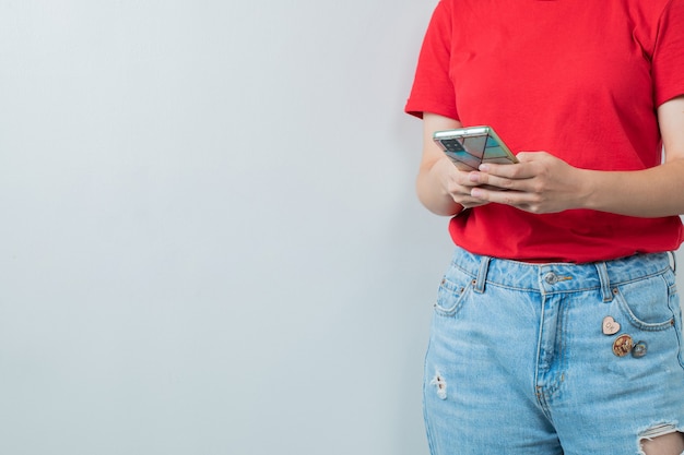 Junges mädchen im roten hemd, das ein silbernes smartphone hält