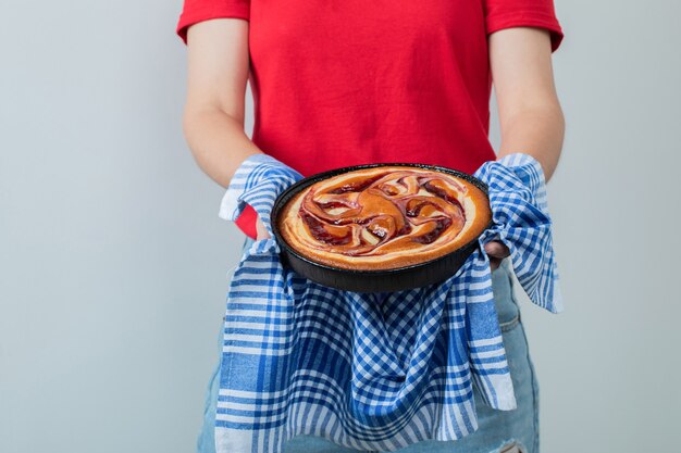 Junges Mädchen im roten Hemd, das einen Kuchen in einer schwarzen Pfanne hält