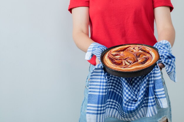 Junges Mädchen im roten Hemd, das einen Kuchen in einer schwarzen Pfanne hält