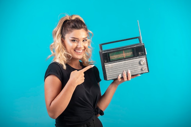 Junges Mädchen im schwarzen Hemd, das ein Vintages Radio hält und sich positiv fühlt.