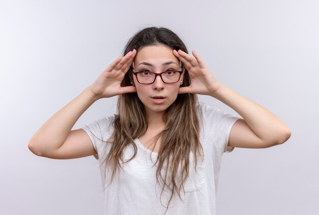 Junges Mädchen im weißen T-Shirt, das Augen mit den Händen öffnet, die versuchen, besser zu sehen