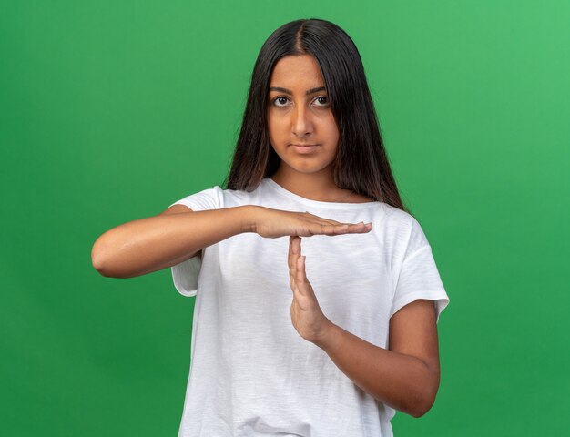 Junges Mädchen im weißen T-Shirt, das mit ernstem Gesicht in die Kamera schaut und eine Auszeitgeste mit den Händen macht