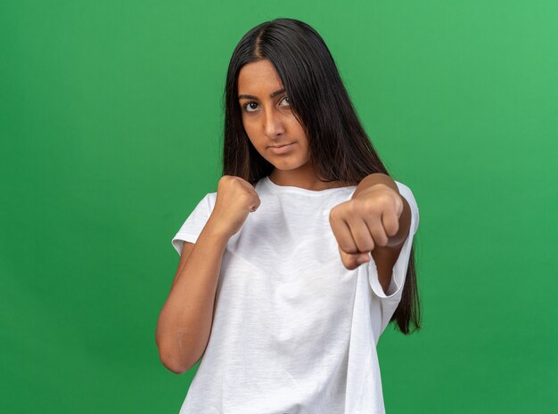 Junges Mädchen im weißen T-Shirt, das mit geballten Fäusten in die Kamera schaut und wie ein Boxer mit ernstem Gesicht posiert