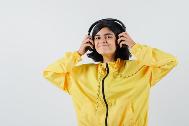 Junges Mädchen in der gelben Bomberjacke, die Musik mit Kopfhörern hört und lächelt und glücklich schaut