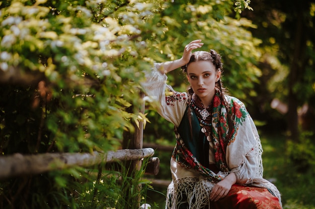 Kostenloses Foto junges mädchen in einem traditionellen ukrainischen kleid sitzt auf einer bank im park