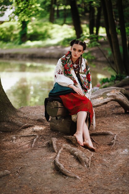 Junges Mädchen in einem ukrainischen gestickten Kleid, das auf einer Bank nahe dem See sitzt