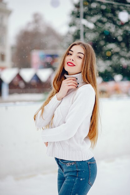 Junges Mädchen in einer weißen Strickjacke, die in einem Winterpark steht