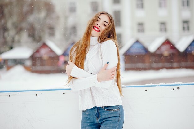 Junges Mädchen in einer weißen Strickjacke, die in einem Winterpark steht