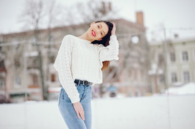 Junges Mädchen in einer weißen Strickjacke, die in einem Winterpark steht