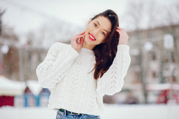 Junges Mädchen in einer weißen Strickjacke, die in einem Winterpark steht