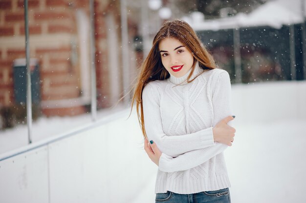 Junges Mädchen in einer weißen Strickjacke, die in einem Winterpark steht