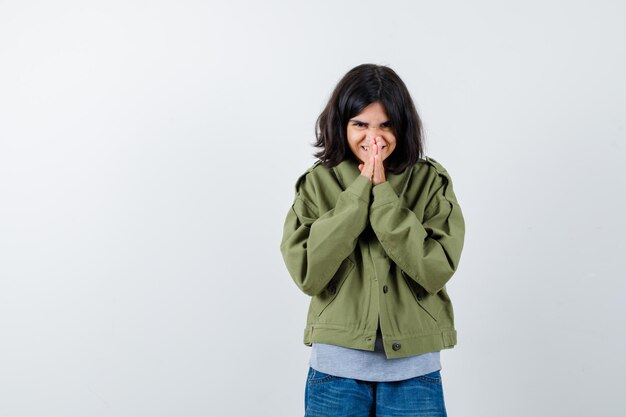 Junges Mädchen in grauem Pullover, Khaki-Jacke, Jeanshose, die Namaste-Geste zeigt und süß aussieht, Vorderansicht.