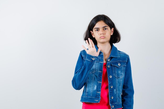 Junges Mädchen in rotem T-Shirt und Jeansjacke mit Stoppschild und ernstem Blick