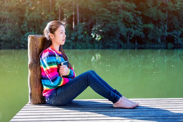 Junges Mädchen mit einem Buch, das auf einem Pier sitzt.