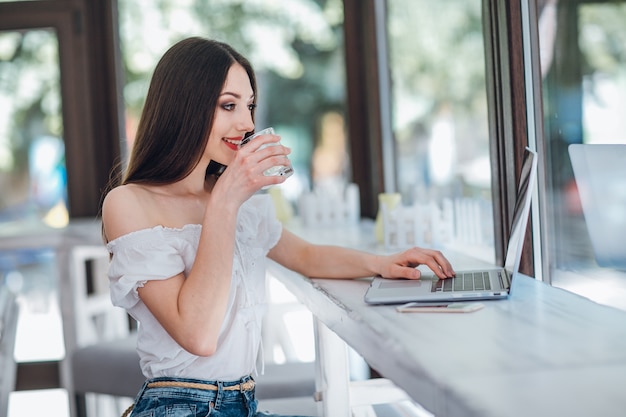 Junges Mädchen mit einem Glas in der Hand und einem Laptop neben ihm lächelnd