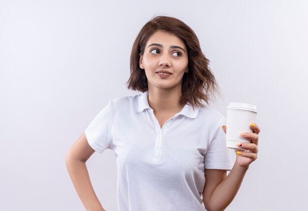 Junges Mädchen mit kurzen Haaren, die weißes Poloshirt tragen, das Kaffeetasse hält lächelnd beiseite schaut