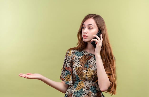 Junges Mädchen mit langen Haaren, die buntes Kleid tragen, das verwirrt spricht, während auf Handy spricht