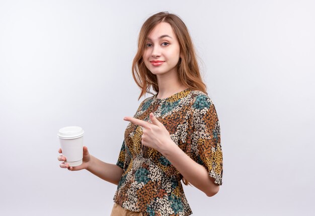 Junges Mädchen mit langen Haaren, die buntes Kleid tragen Kaffeetasse halten, die mit Finger darauf zeigt