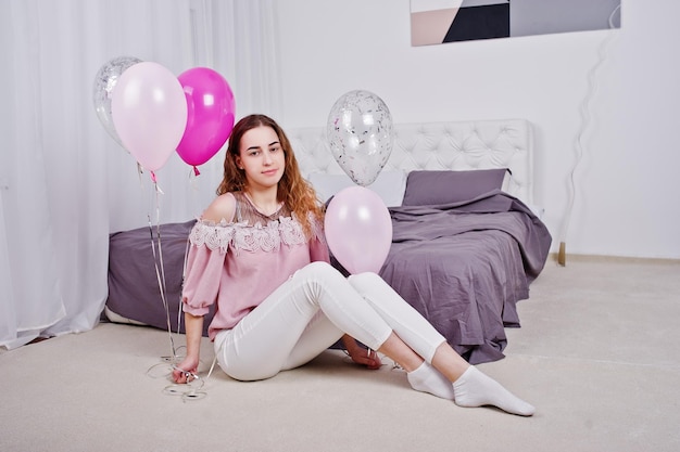 Junges Mädchen mit Luftballons auf dem Bett posiert im Studiozimmer