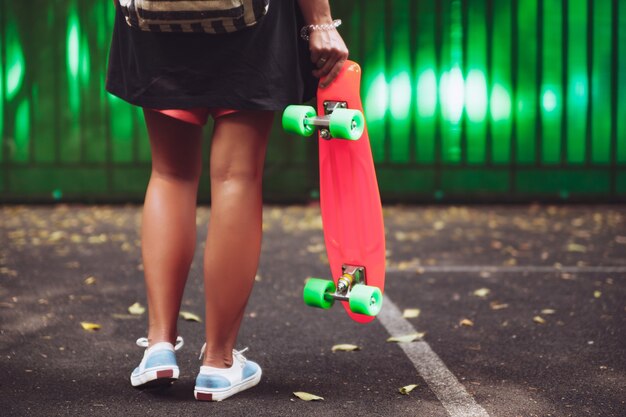 Junges Mädchen mit Plastik orange Penny Shortboard hinter grüner Wand in Kappe