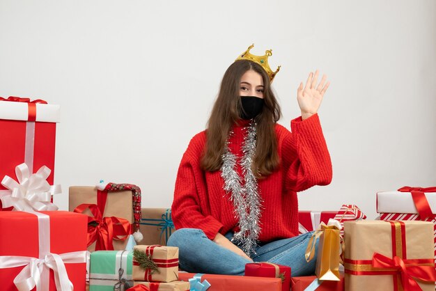 junges Mädchen mit rotem Pullover, der ihre Hand hebt, die um Geschenke mit schwarzer Maske auf Weiß sitzt