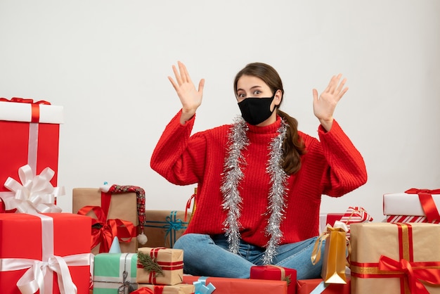 junges Mädchen mit rotem Pullover opning ihre Hände sitzen um Geschenke auf weiß