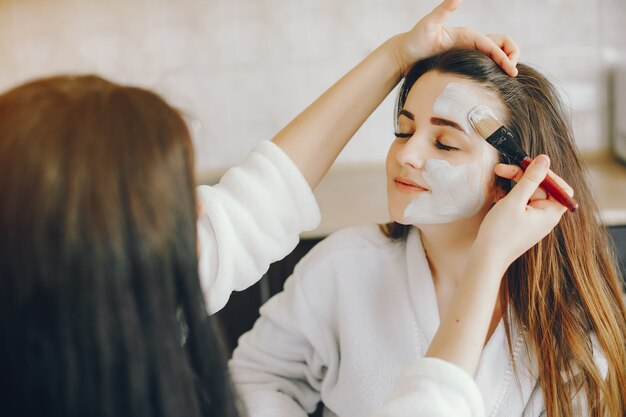 junges Mädchen mit schönen Händen legt eine erfrischende Maske auf das Gesicht ihrer Freundin mit einem Pinsel