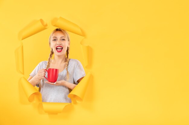 Junges Mädchen mit Tasse Tee auf einem zerrissenen gelben Papierhintergrund, der das Einkaufen annonciert