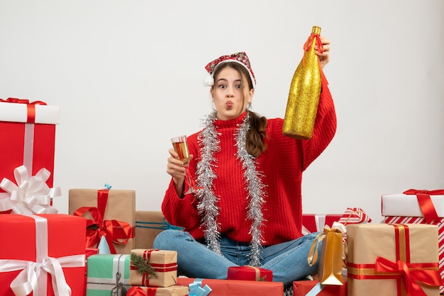 junges Mädchen mit Weihnachtsmütze, die Champagner und Glas hält, die herum Geschenke auf Weiß sitzen