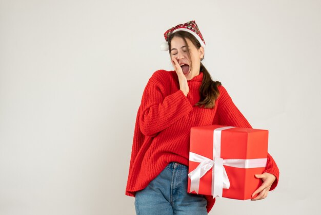 junges Mädchen mit Weihnachtsmütze, die Geschenk hält, das auf Weiß steht