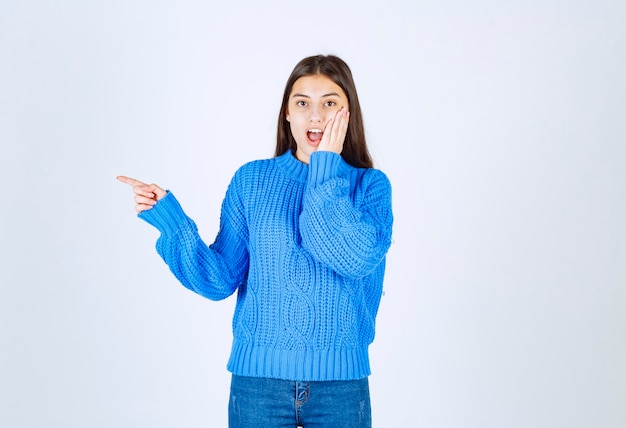 junges Mädchen-Modell im blauen Pullover, der auf weiß-grau zeigt.