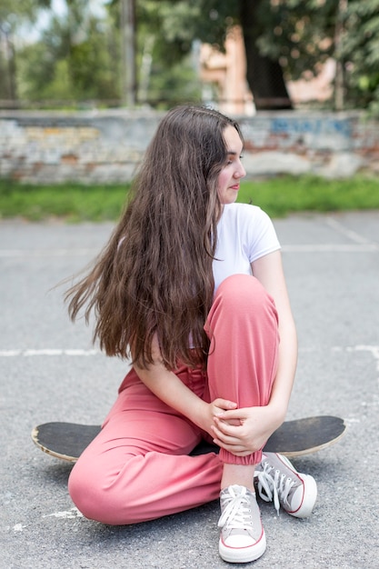 Junges Mädchen posiert beim Sitzen auf ihrem Skateboard