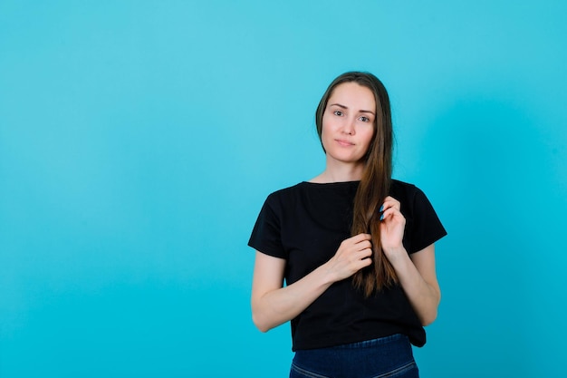 Junges mädchen schaut in die kamera, indem es haare auf blauem hintergrund hält