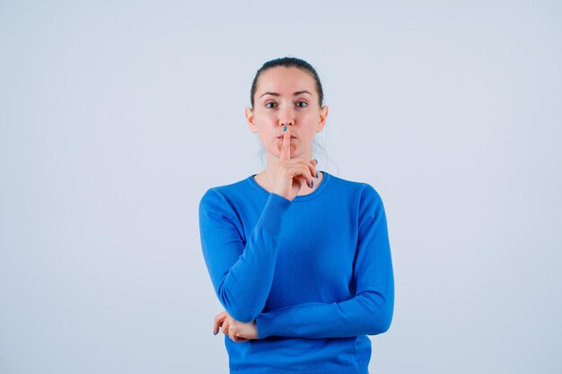 Junges Mädchen schaut in die Kamera, indem sie den Zeigefinger auf den Lippen auf weißem Hintergrund hält