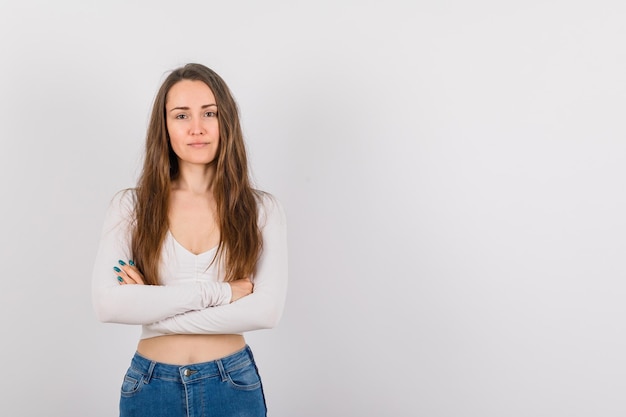 Junges Mädchen schaut in die Kamera, indem sie die Arme auf weißem Hintergrund kreuzt