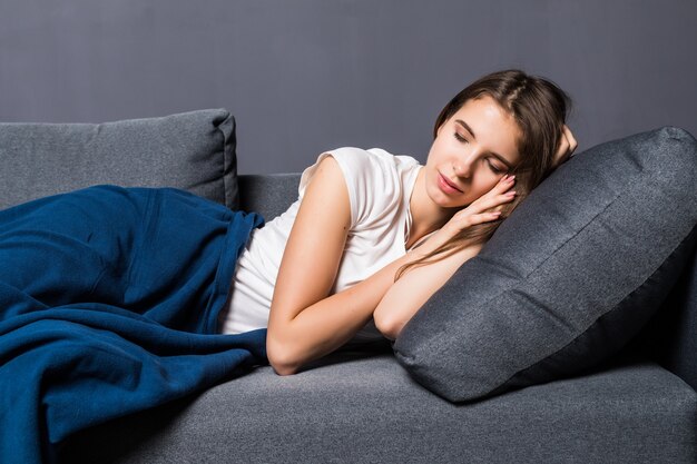 Junges Mädchen schlafend auf einem Sofa bedeckt mit blauer Bettdecke auf grauem Hintergrund