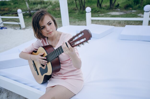 Junges Mädchen sitzt auf einem Bett, Gitarre zu spielen