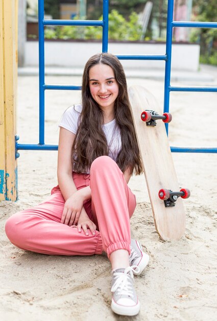 Junges Mädchen sitzt neben Skateboard draußen