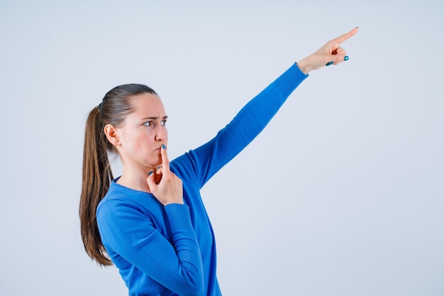 Junges Mädchen zeigt mit dem Zeigefinger nach oben und legt den anderen Zeigefinger auf die Lippen auf weißem Hintergrund