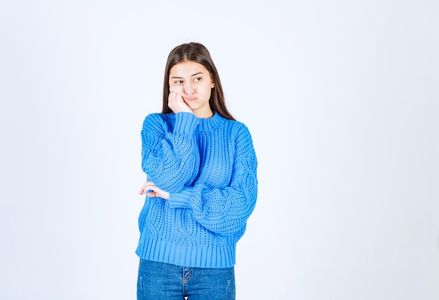 junges Mädchenmodell im blauen Pullover, der auf weiß-grau steht und posiert.