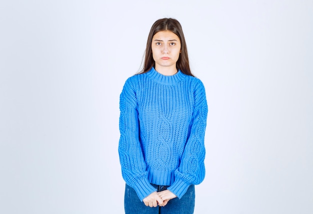 junges Mädchenmodell im blauen Pullover, der auf weiß-grau steht und posiert.