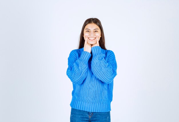junges Mädchenmodell im blauen Pullover, der auf weiß-grau steht und posiert.