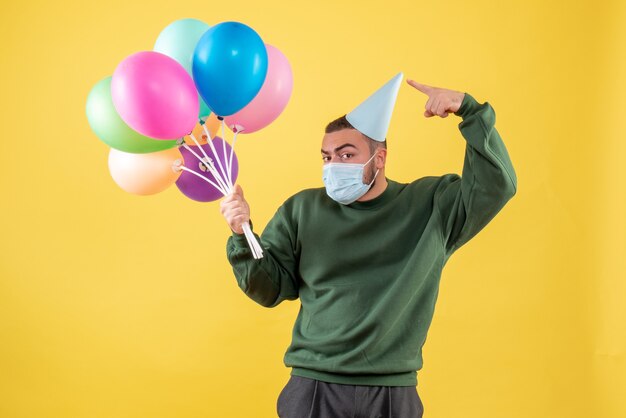 Junges Männchen der Vorderansicht, das bunte Ballons auf gelbem Hintergrund hält