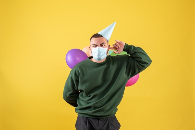 Junges Männchen der Vorderansicht, das bunte Ballons auf gelbem Hintergrund hält