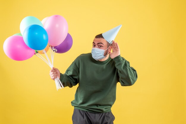 Junges Männchen der Vorderansicht, das bunte Ballons auf gelbem Hintergrund hält