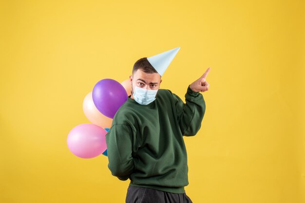 Junges Männchen der Vorderansicht, das bunte Ballons auf gelbem Hintergrund hält