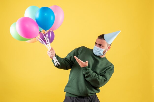 Junges Männchen der Vorderansicht, das bunte Ballons auf gelbem Hintergrund hält